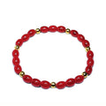 Red glass beaded bracelet with gold brass accents sitting on a white background