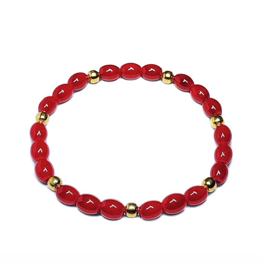 Red glass beaded bracelet with gold brass accents sitting on a white background