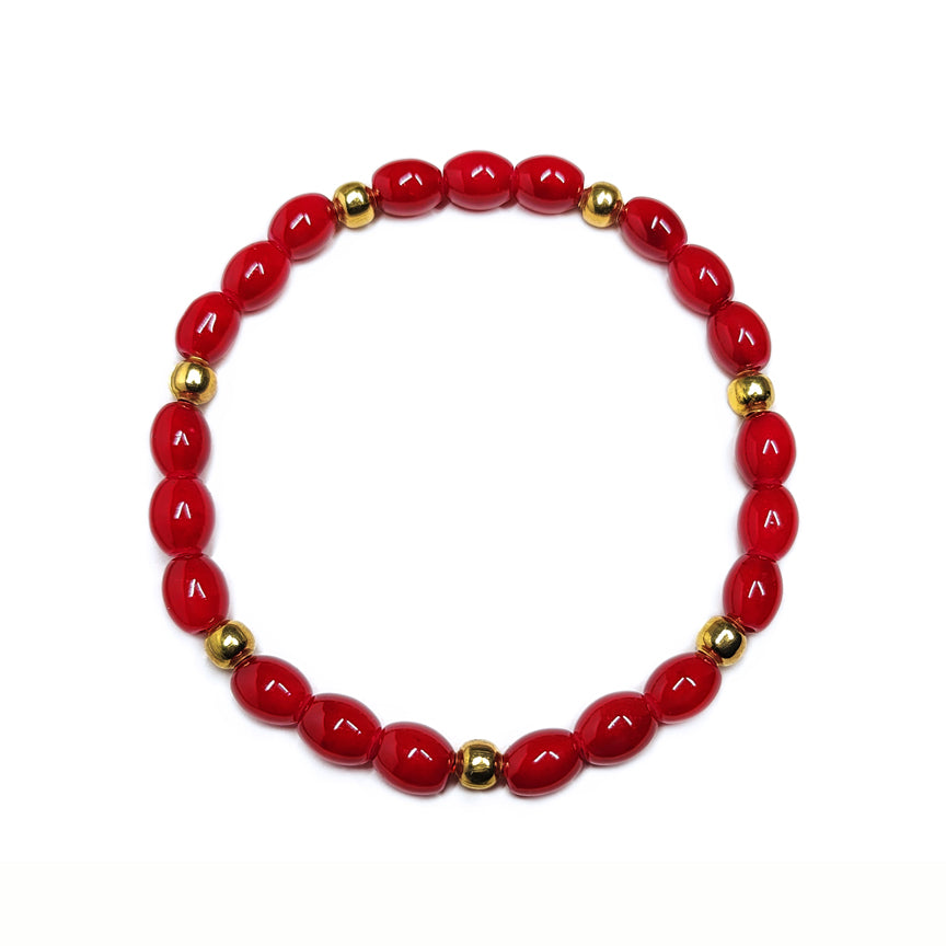 Red glass beaded bracelet with gold brass accents floating over a white background